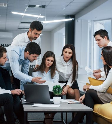 Guy shows document to a girl. Group of young freelancers in the office have conversation and working.